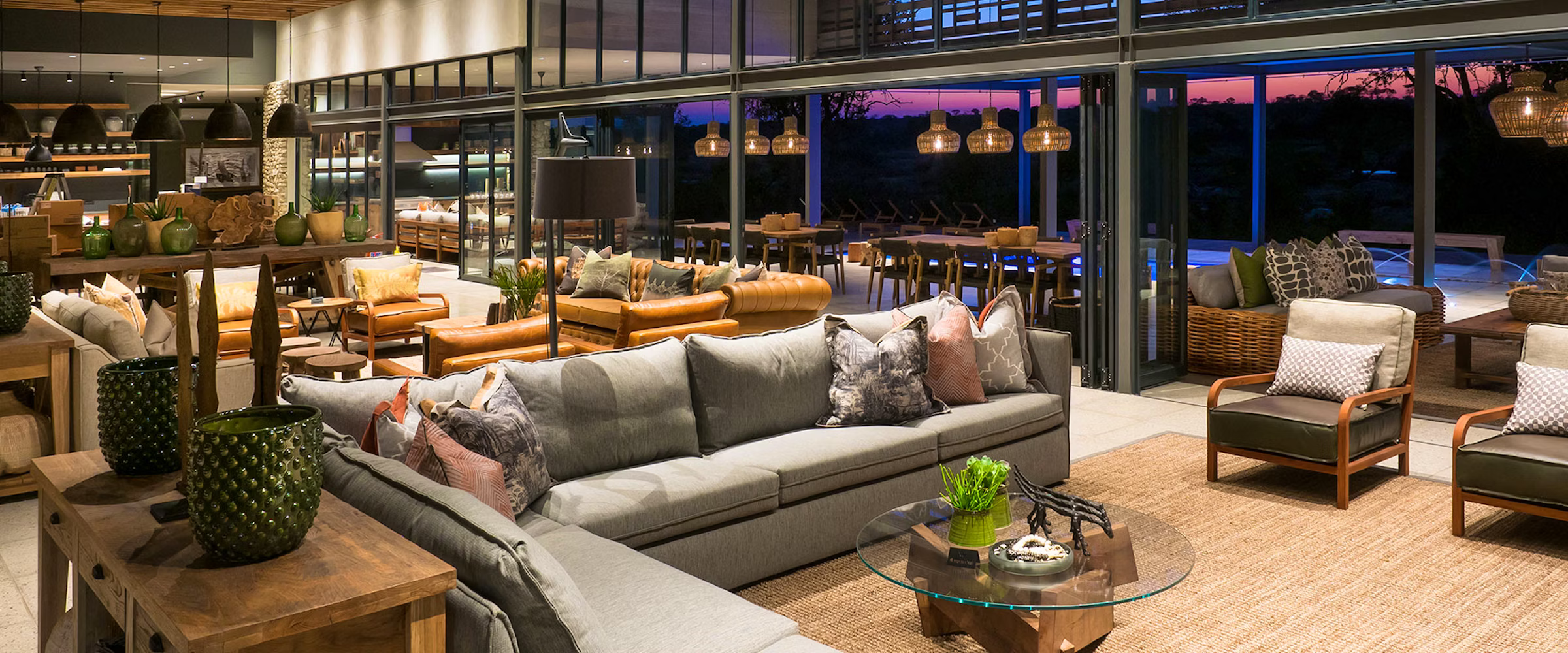 A luxurious lounge at Kruger Safari Lodge featuring plush seating, elegant decor, and large glass doors opening to a sunset view. The space blends modern design with natural elements, highlighting comfort and style in a safari setting.