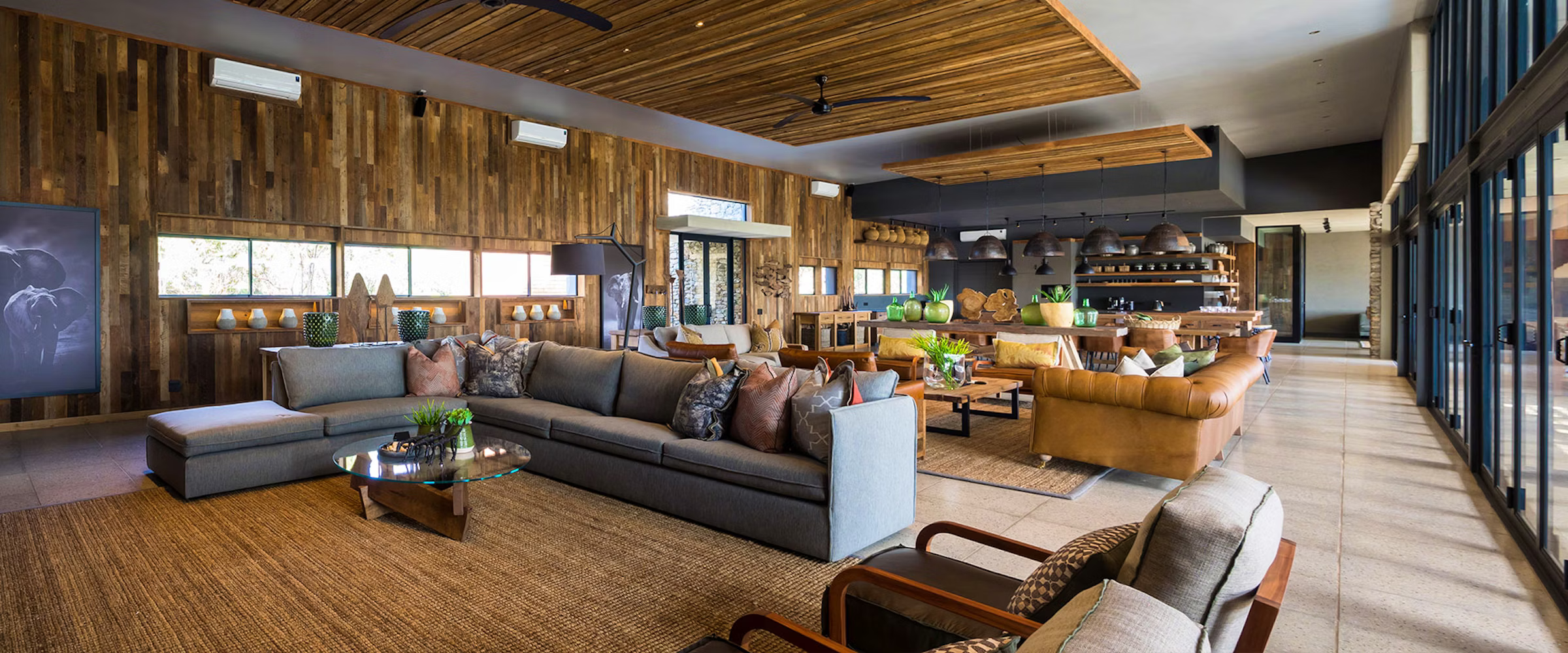 A spacious, elegant lounge at Kruger Safari Lodge featuring modern architecture, plush seating, and wooden accents. Large windows provide natural light, enhancing the luxurious ambiance designed for relaxation and wildlife viewing in Kruger National Park.