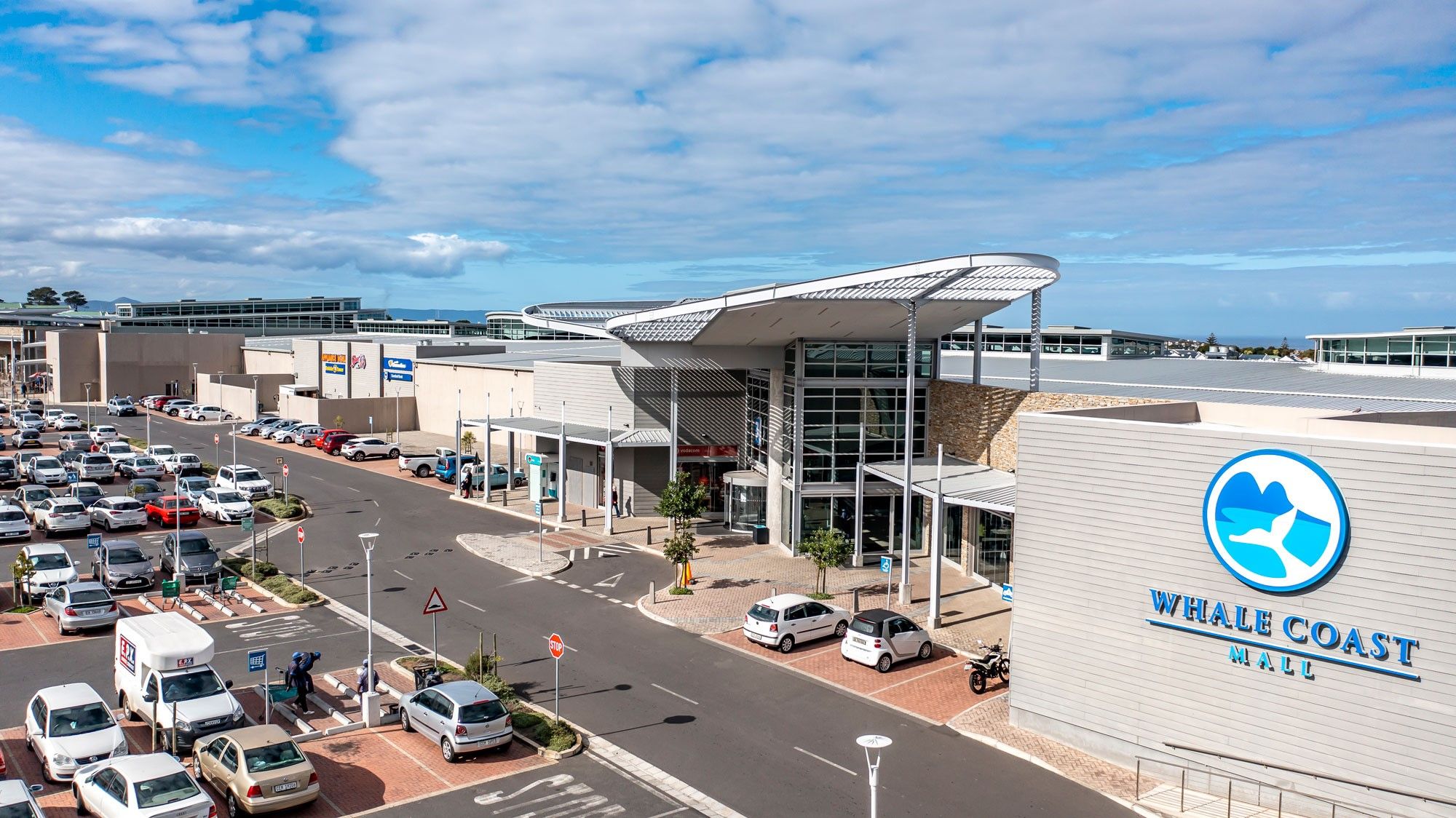 Aerial view of Whale Coast Mall, showcasing its modern design and expansive parking area. The mall serves as a primary shopping destination on the Whale Coast, offering a variety of stores, restaurants, and services. The setting highlights accessibility and convenience for locals and visitors.